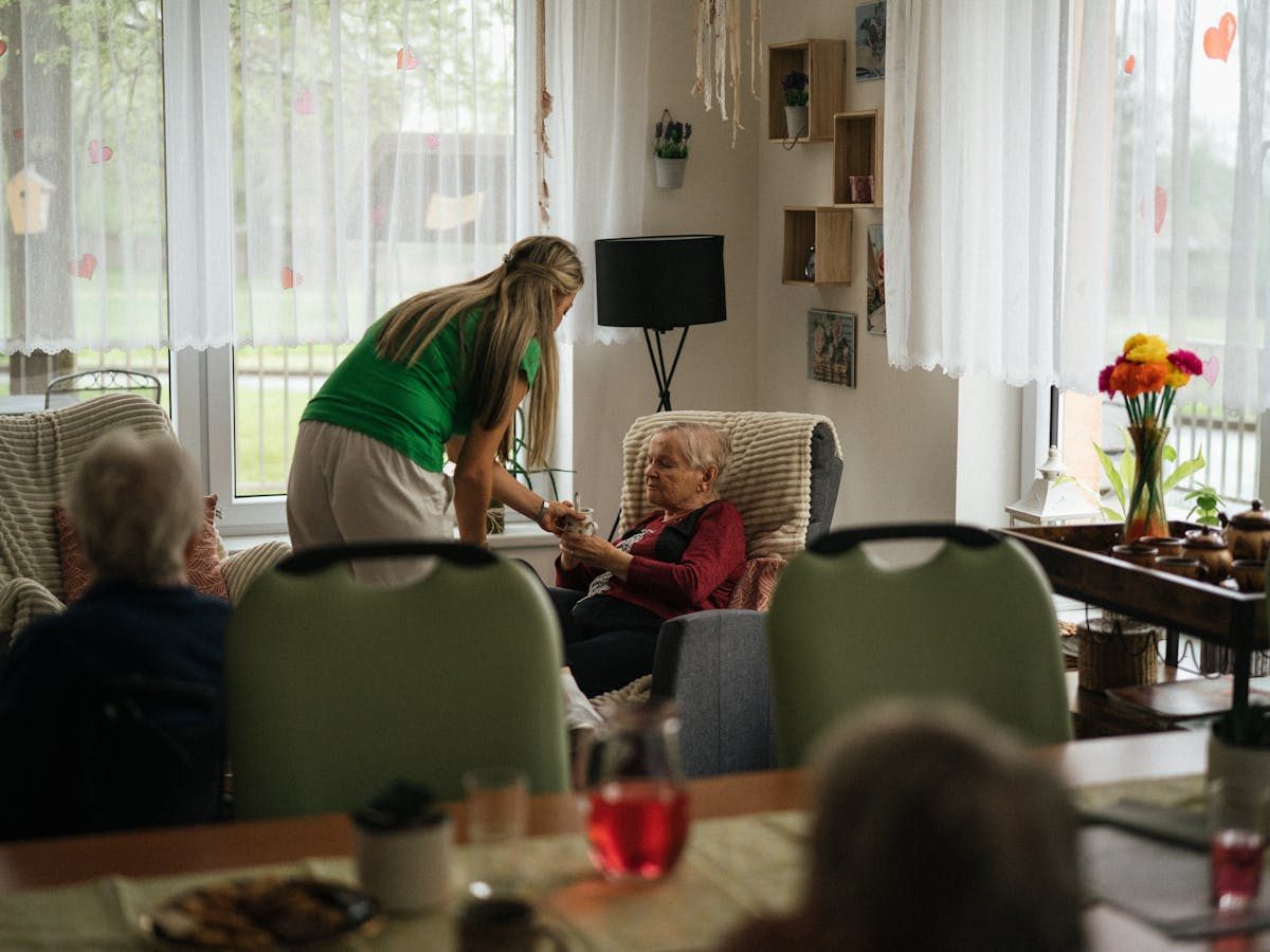 Soignante et résidents âgés autour d'une table devant de grandes baies vitrées